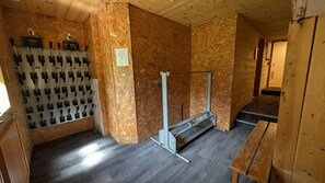 Una habitación con suelo de madera, un banco de metal, un estante con diferentes herramientas y una puerta de madera.