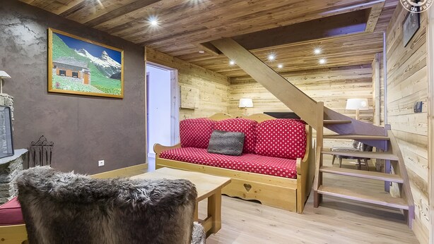 Un interior acogedor de madera, con un sofá rojo, una mesa de madera y una escalera.