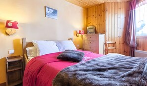 A bedroom with a bed, wooden walls, a dresser, and a window with curtains. - “Chalet Le Névé - Le Tétras-Lyre” with Mountain View, Heated Pool, 150m from the Slopes (Bonneval-sur-Arc)