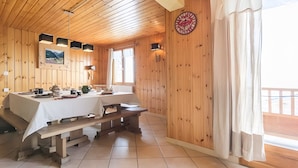 Interior de madera con una mesa de comedor lista para cuatro personas, un banco y un reloj en la pared.