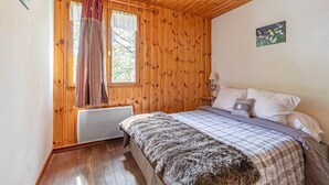 Un dormitorio con paredes de madera, una cama con manta a cuadros, una ventana con cortinas y una mesita de noche pequeña con una lámpara.