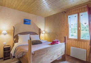 A wooden-paneled room with a bed, two wall-mounted lamps, a window with a view, and a small table. - Chalet Le Névé - Perce Neige Apartment with Mountain View, Heated Pool (Bonneval-sur-Arc)