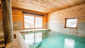 Interior de una cabaña de madera con piscina, paredes de piedra y grandes ventanales.