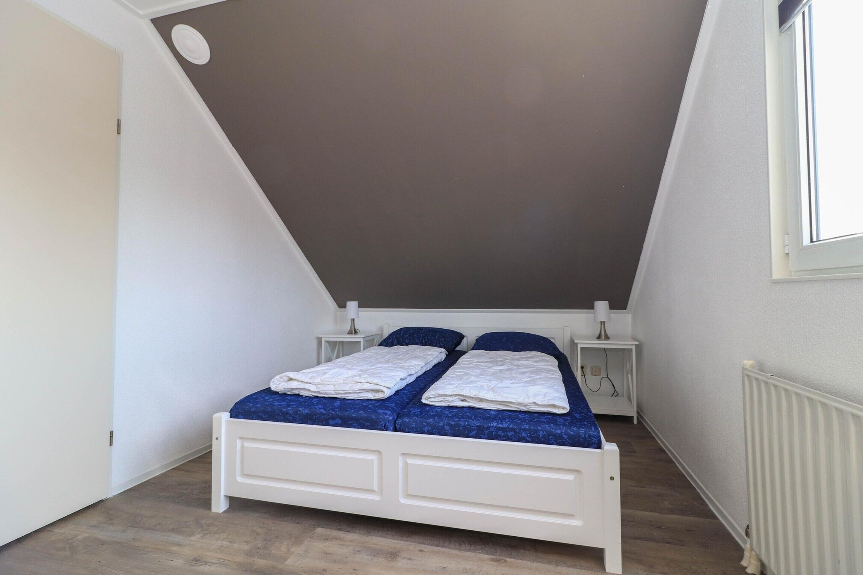 Ein kleines Zimmer mit einem Einzelbett, geneigter Decke, weißen Wänden und einem Fenster.