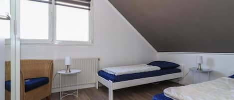 Een slaapkamer met een schuine plafond, twee bedden, een klein tafeltje, een stoel en een radiator.