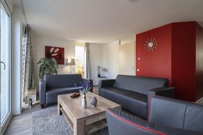 A modern living room with two sofas, a coffee table, and a red accent wall. - Deluxe Comfy Waterfront Bungalow (Makkum)