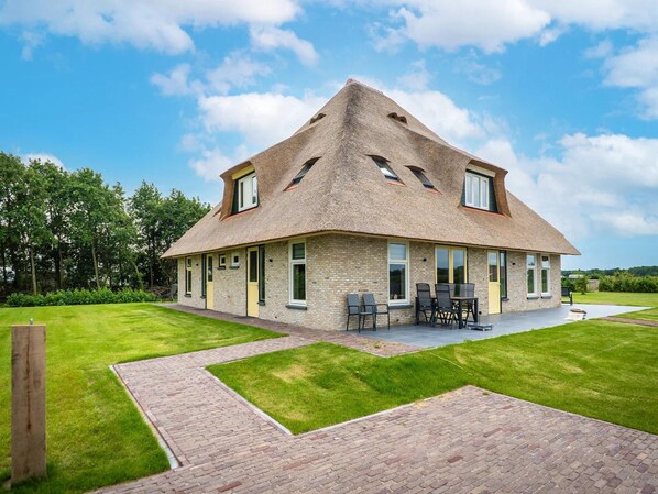 A house with a steeply pitched roof, multiple windows, and a paved patio area with outdoor furniture. - Farmhouse Near De Koog (De Koog)