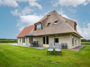 Ein Haus mit einem geneigten Dach, einer Terrasse mit Stühlen und einem Rasen.