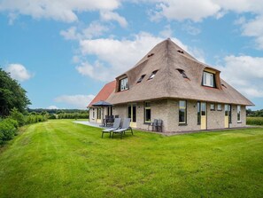 A modern house with a sloped roof, a well-maintained lawn, and a patio with outdoor furniture. - Farmhouse Near De Koog (De Koog)