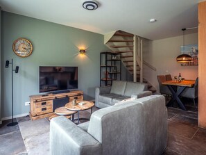 Ein modernes Wohnzimmer mit Flachbildfernseher, grauen Sofas, einem Holztisch, einem Bücherregal und einer Treppe.