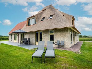 Una casa con tetto spiovente, un patio con sedie e un prato verde.