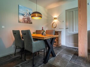 A dining area with a wooden table, four chairs, a pendant light, and a wall-mounted light fixture. - Farmhouse Near De Koog (De Koog)