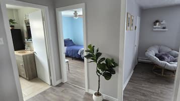 A room with a grey tiled floor, a white door leading to another room, a potted plant, and a grey rocking chair.