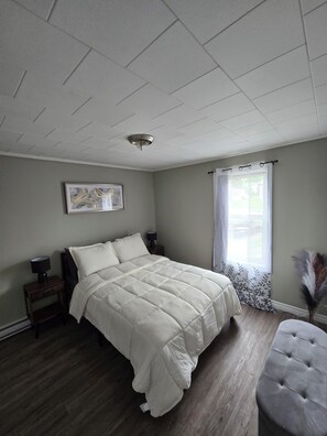 A bedroom with a bed, bedside tables, a ceiling light, a window with curtains, and a wall-mounted picture. - Heart of Town Near Falls (Grand Falls)