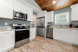 A modern kitchen with white cabinetry, stainless steel appliances, and a wooden ceiling. - Beautiful 4-bedroom house with AC in quaint Waveland (Waveland)