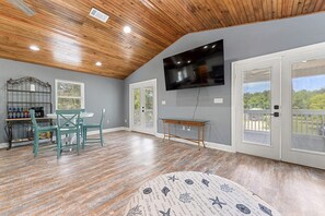 A room with a wooden ceiling, a flat-screen TV mounted on the wall, a dining table with chairs, and a window with blinds. - Beautiful 4-bedroom house with AC in quaint Waveland (Waveland)