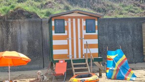 A beach house with a small deck, a beach chair, a dog, and a colorful beach umbrella. - Beach Cottage With Hut for 9 (Pwllheli)