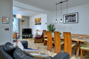 A modern living room with a sofa, a TV, a dining table with chairs, and artwork on the walls.