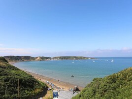 A coastal beach with clear skies, a sandy shore, and boats in the water.