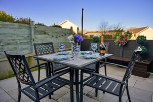 Un patio exterior con una mesa dispuesta para cuatro, incluyendo platos, vasos y una botella de vino.
