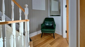 A staircase with white balusters and a wooden handrail, leading to a room with a green velvet chair and a mirror on the wall. - Beach Cottage With Hut for 9 (Pwllheli)