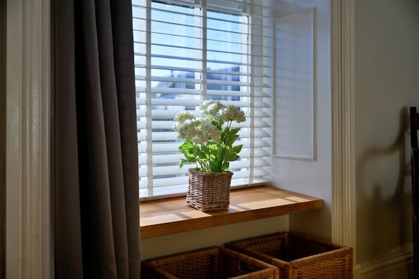 A window with white blinds, a wicker basket with white flowers, and two wicker baskets on a wooden ledge. - Beach Cottage With Hut for 9 (Pwllheli)