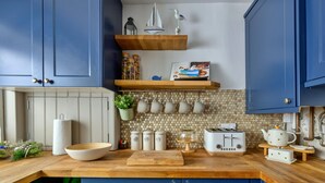 A kitchen with blue cabinets, a wooden countertop, a toaster, and a hanging pot rack. - Beach Cottage With Hut for 9 (Pwllheli)