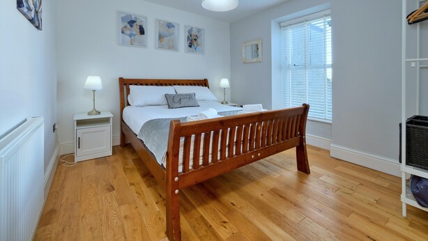 A bedroom with a wooden bed, white walls, and a window with blinds. - Beach Cottage With Hut for 9 (Pwllheli)