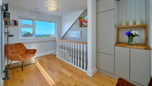 A modern interior with a wooden floor, a white staircase, a view through a window, and a bookshelf. - Beach Cottage With Hut for 9 (Pwllheli)
