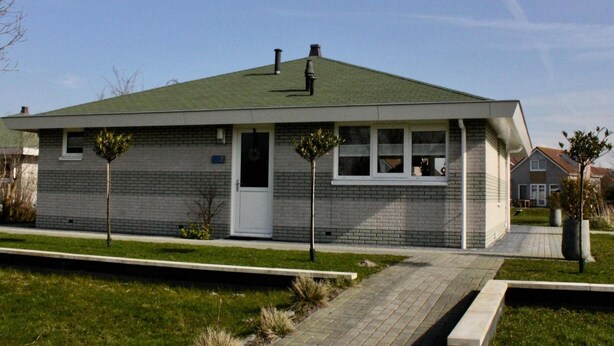 Eenlaags bakstenen huis met een groen dak, een voordeur en een klein voortuintje.