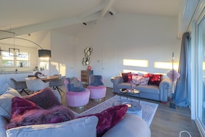 Ein modernes Wohnzimmer mit einer grauen Sofagarnitur, einem Essbereich mit rundem Tisch und einer Küche im Hintergrund.