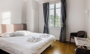 Ein Hotelzimmer mit Bett, Stuhl, einem Fenster mit Vorhängen und einer Tür.