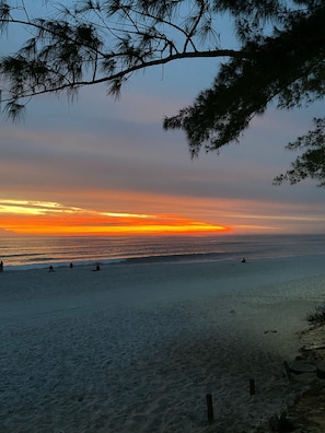 A beach with a sunset, ocean waves, and people on the sand.