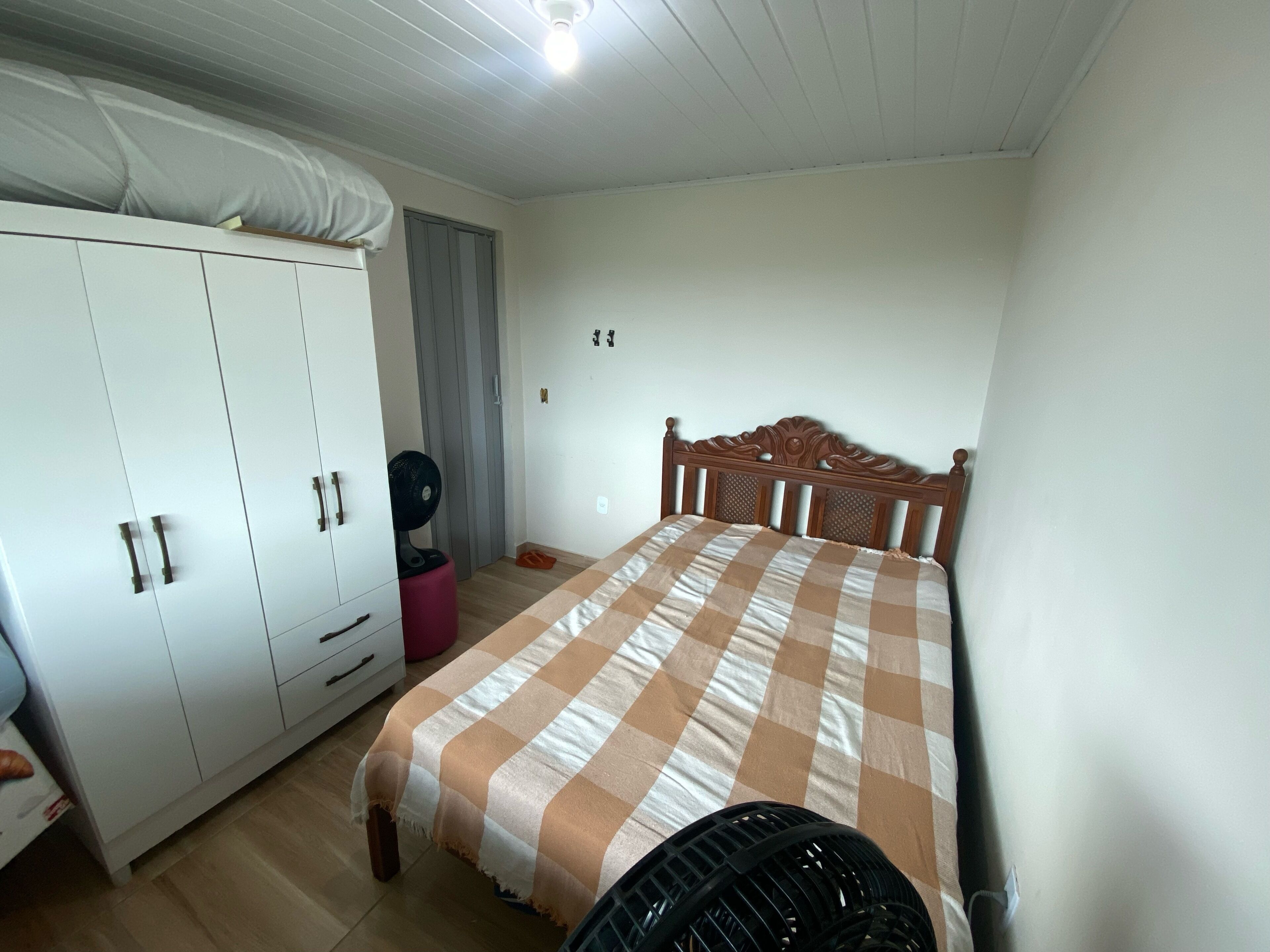 A bedroom with a bed, wardrobe, and a standing fan.