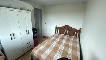 A bedroom with a bed, wardrobe, and a standing fan.