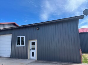 A single-story building with a grey exterior, a white garage door, and a small window. - Stay in Style 1Br/1Bath Barndominium Northown Escanaba (Escanaba)