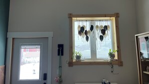 Um quarto com janela, porta, uma pequena prateleira com uma planta e um objeto decorativo na parede.
