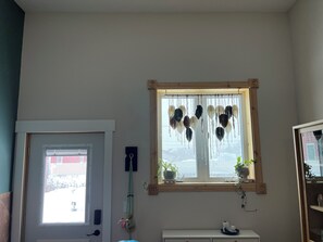 A room with a window, a door, a small shelf with a plant, and a wall-mounted decoration. - Stay in Style 1Br/1Bath Barndominium Northown Escanaba (Escanaba)