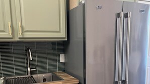 Uma cozinha com armários verde-claros, uma geladeira de aço inoxidável, bancada de madeira e uma pia moderna.