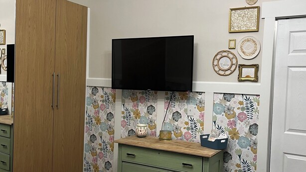 Um quarto com uma cama, um guarda-roupa, uma cômoda, uma televisão e uma porta.