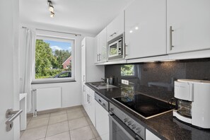 A modern kitchen with white cabinets, a built-in microwave, a stove, and a window overlooking a residential area.