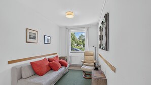 Una habitación con sofá, sillón, una mesita y ventana con vistas al exterior.