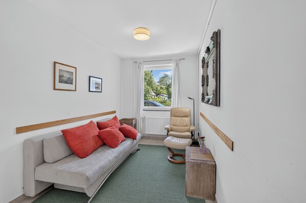 A room with a sofa, a chair, a small table, and a window with a view of the outside.