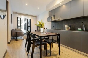 A modern kitchen with dark cabinetry, a dining table with chairs, and a potted plant on the table. - Charming 1-bedroom apartment in the heart of Interlomas (Naucalpan de Juárez)