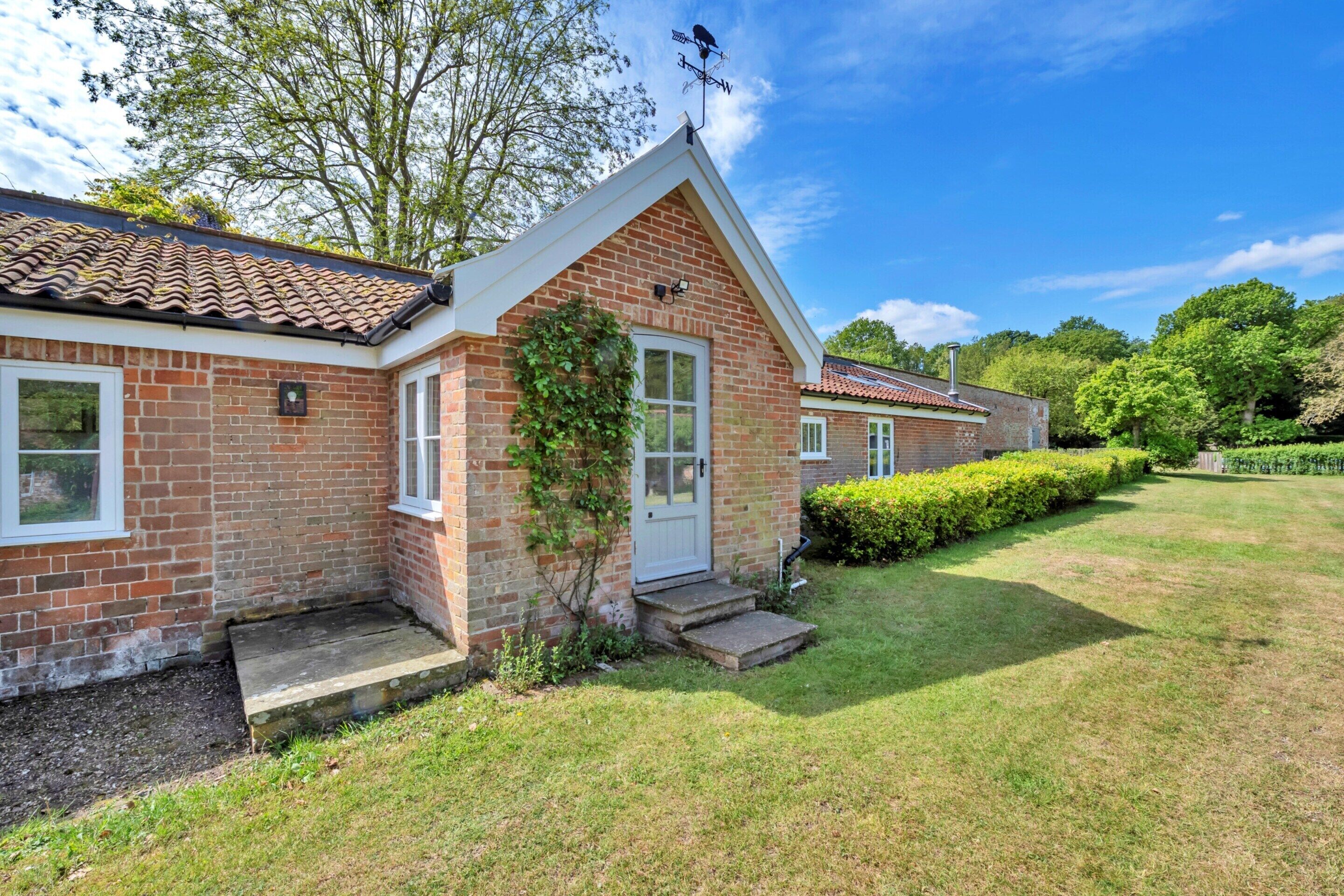 A brick house with a tiled roof, a front door, and a small front yard with a hedge.
