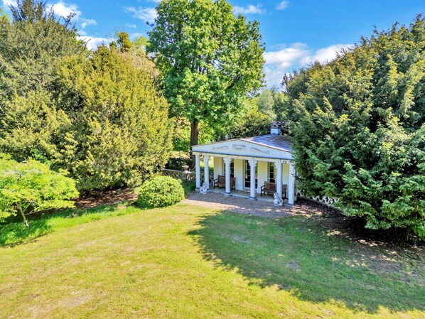 A gazebo with a white exterior and columns, surrounded by lush greenery and trees.