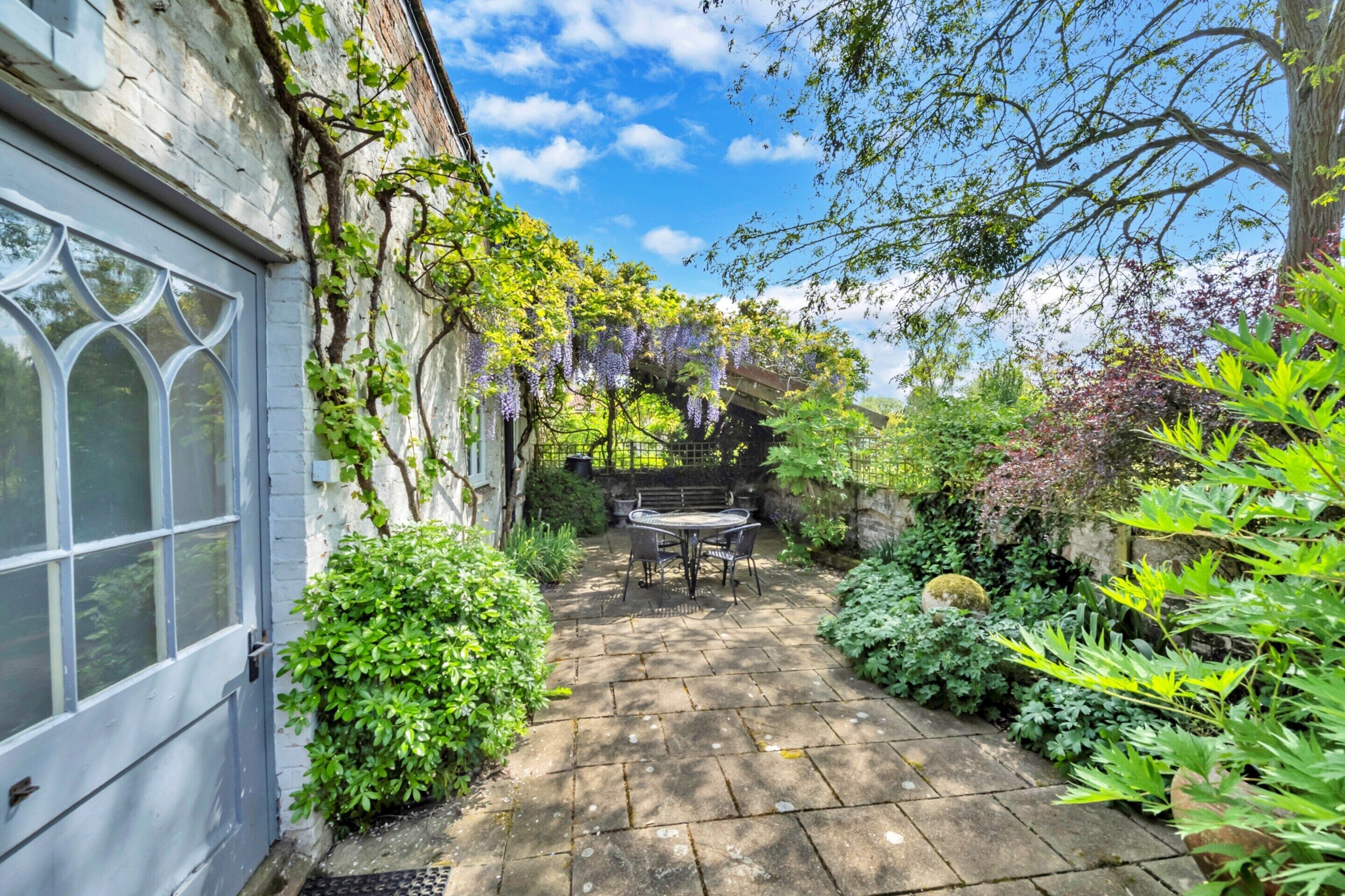 A garden with a stone patio, a table and chairs, and a building with a window.