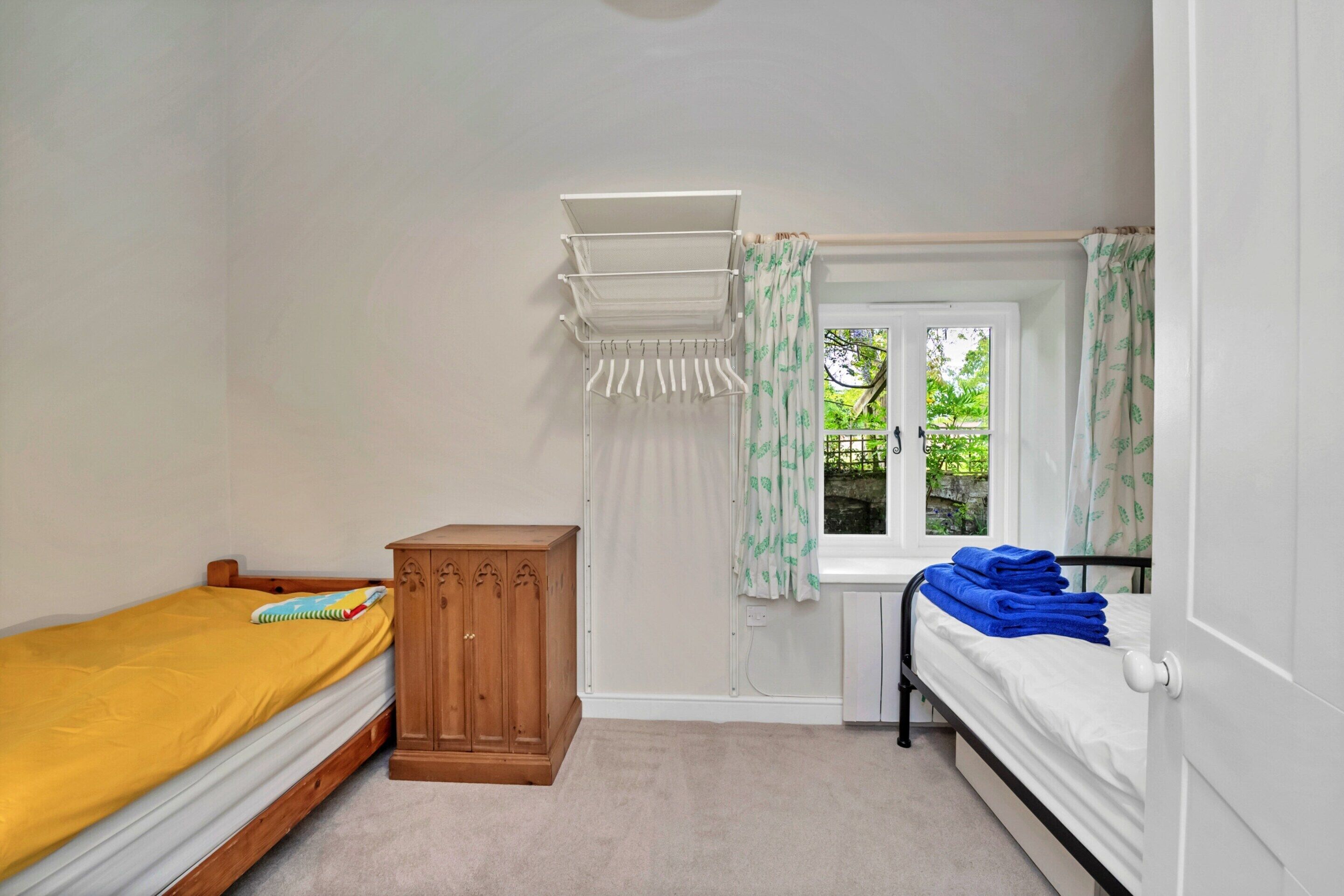 Une chambre avec deux lits, une armoire en bois, une fenêtre avec des rideaux et un étendoir à linge.