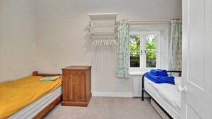 A bedroom with two beds, a wooden wardrobe, a window with curtains, and a hanging laundry rack.