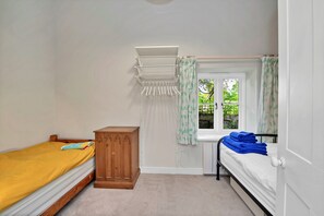 A bedroom with two beds, a wooden wardrobe, a window with curtains, and a hanging laundry rack.